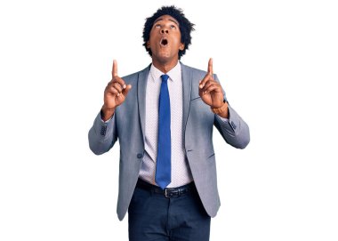 Afro saçlı, iş ceketi giyen yakışıklı afro-amerikalı adam şaşkın şaşkın yukarı bakıyor ve parmaklarıyla işaret ediyor ve kollarını kaldırıyor.. 