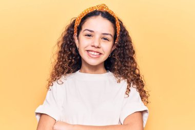 Kıvırcık saçlı, sıradan giyinen, mutlu yüzlü, kollarını kavuşturup kameraya bakan güzel bir kız. pozitif kişi. 