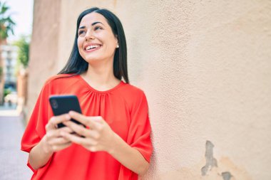 Genç Latin kız şehirde akıllı telefon kullanarak mutlu bir şekilde gülümsüyor..