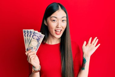 Japon yen banknotları tutan genç Çinli kadın başarıyı mutlu bir gülümsemeyle kutluyor ve kazanan el kaldırarak ifade ediyor. 