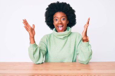 Sıradan bir kazak giyen genç Afro-Amerikalı kadın zaferi mutlu bir gülümsemeyle ve ellerini kaldırarak kazanan ifadeyle kutluyor. 