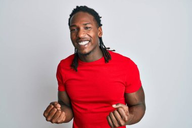 Saçları örgülü, mutlu ve heyecanlı Afrika kökenli Amerikalı bir adam kolları havada, gülümseyen ve başarı için bağıran, kazanan bir jest yapıyor. kutlama konsepti. 