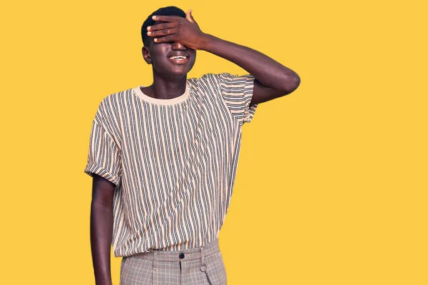カジュアルな服を着た若いアフリカ系アメリカ人の男性が笑顔で 驚きのために目を覆う顔で笑っています 視覚障害の概念 — ストック写真