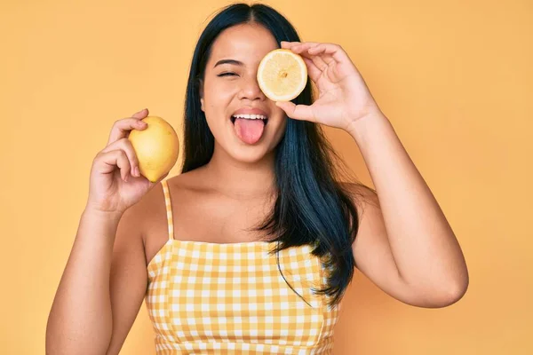 年轻美丽的亚洲女孩牵着柠檬伸出舌头 带着滑稽的表情高兴极了 — 图库照片