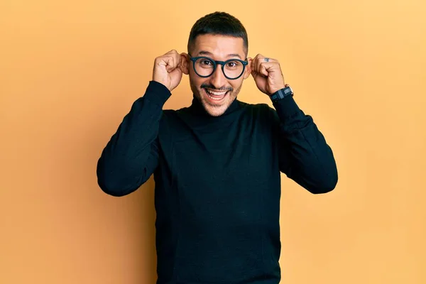 タトゥーネックのセーターと眼鏡を着てハンサムな男は 指で耳を引く笑みを浮かべて 面白いジェスチャー オーディション問題 — ストック写真