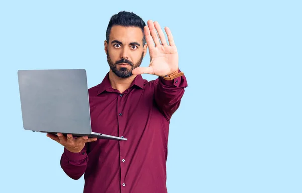 Jovem Hispânico Homem Segurando Laptop Com Mão Aberta Fazendo Sinal — Fotografia de Stock