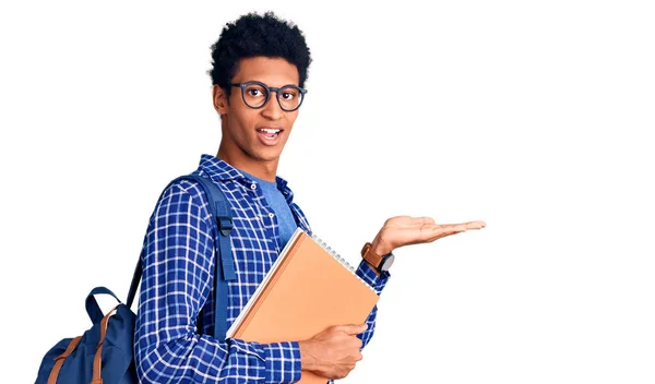 Joven Afroamericano Hombre Usando Estudiante Mochila Celebración Libro Apuntando Lado —  Fotos de Stock