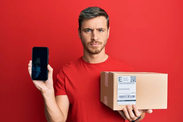 Knappe Blanke Man Houdt Levering Pakket Toont Smartphone Scherm Sceptisch — Stockfoto