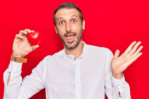 Jovem Homem Bonito Segurando Coração Celebrando Realização Com Sorriso Feliz — Fotografia de Stock