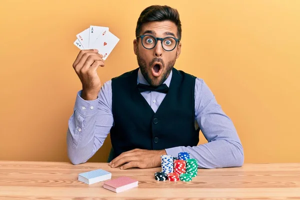 英俊的惊慌失措的男人坐在桌子上 手里拿着扑克牌和扑克牌 惊慌失措地张开嘴 满脸诧异 — 图库照片