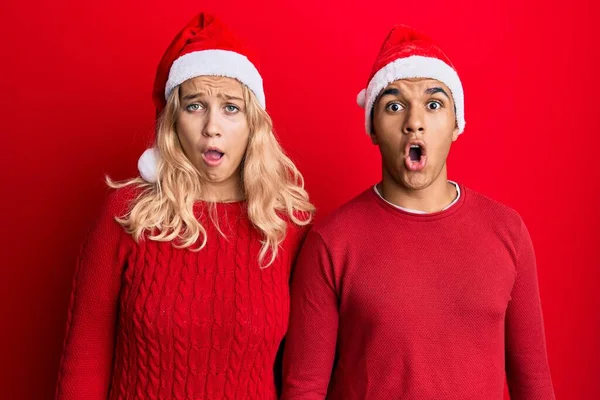 Yılbaşı şapkası takan ırklar arası genç bir çift şaşkınlık ve şaşkınlık içinde ağzı açık, inançsız bir yüz. 