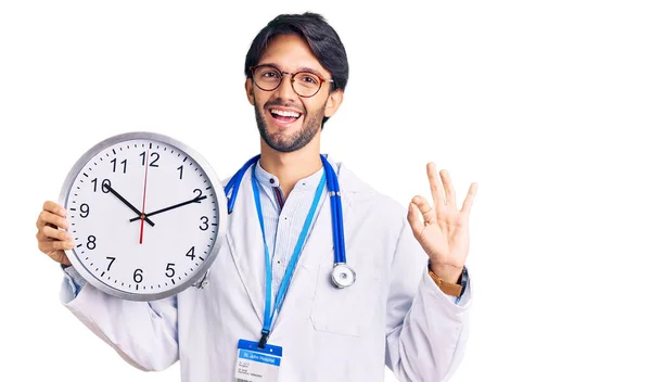 Hombre Hispano Guapo Vistiendo Uniforme Médico Sosteniendo Reloj Haciendo Signo — Foto de Stock