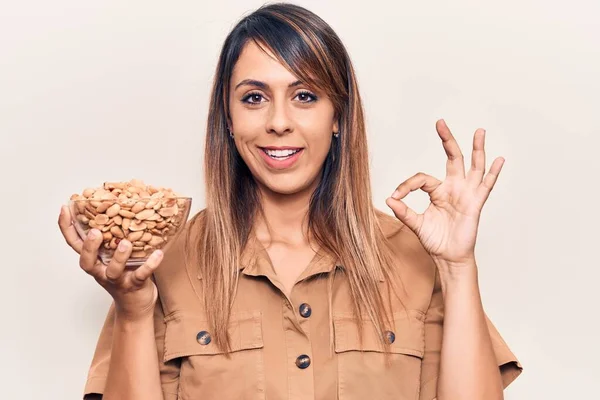 Jovem Bela Mulher Segurando Tigela Com Amendoins Fazendo Sinal Com — Fotografia de Stock