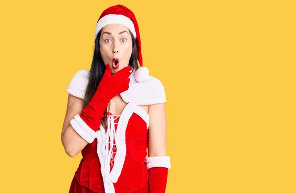 Young beautiful caucasian woman wearing santa claus costume looking fascinated with disbelief, surprise and amazed expression with hands on chin