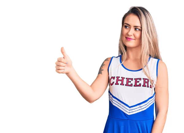 年轻美丽的金发女人穿着啦啦队队长的制服 看上去很自豪 微笑着向旁边竖起大拇指 — 图库照片