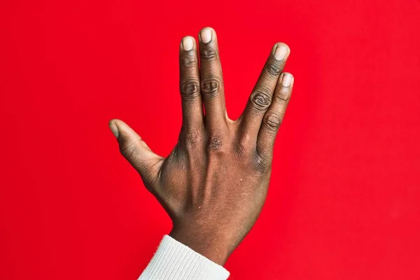 Arm and hand of african american black young man over red isolated background greeting doing vulcan salute, showing back of the hand and fingers, freak culture