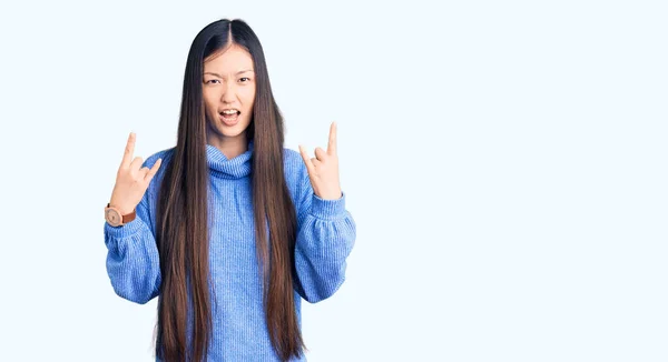 手を上げて岩のシンボルをやって狂気の表情で叫んでカジュアルなタートルネックセーターを身に着けている若い美しい中国の女性 音楽スター 重い概念は — ストック写真