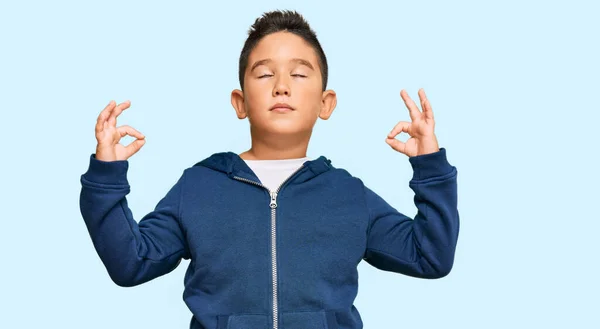 カジュアルなスポーティなジャケットを着た小さな男の子のヒスパニック系の子供は 指で瞑想ジェスチャーを行う閉じて目でリラックスして笑顔 ヨガのコンセプト — ストック写真