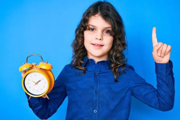 Cute Hispanic Child Long Hair Holding Alarm Clock Surprised Idea — Stock Photo, Image