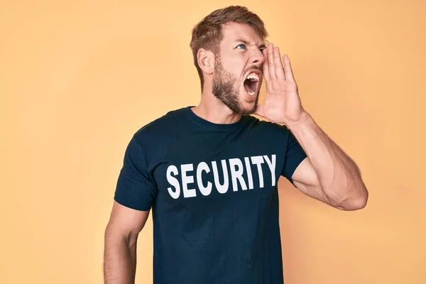 Young caucasian man wearing security t shirt shouting and screaming loud to side with hand on mouth. communication concept.