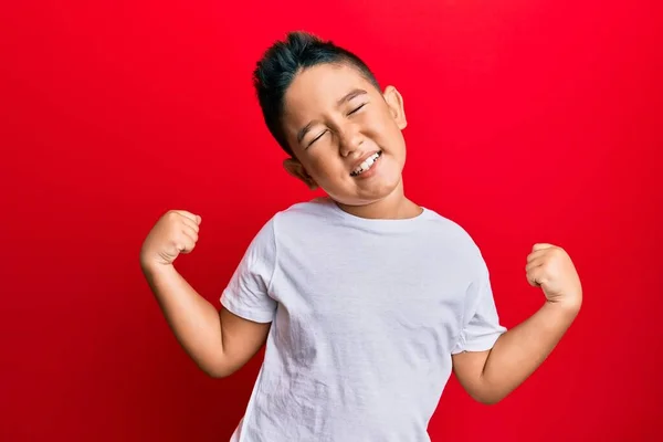 小さな男の子のヒスパニック系の子供は カジュアルな白いTシャツを着て非常に満足し 腕を上げて勝者のジェスチャーを行う興奮し 笑顔と成功のために叫んでいます お祝いのコンセプト — ストック写真