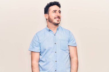 Latin kökenli genç bir adam günlük giysiler giyiyor, rahat bir görünüm takınıyor, doğal bir yüz ifadesi ve kendinden emin bir gülümsemeyle poz veriyor.. 