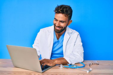 Klinikte çalışan İspanyol üniformalı genç adam pozitif ve mutlu görünüyor. Kendine güvenen bir gülümsemeyle dişlerini gösteriyor. 