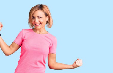 Genç sarışın kadın spor kıyafetleri giyiyor mutlu ve neşeli dans ediyor, gülümsüyor rahat ve kendinden emin bir şekilde müzik dinliyor. 