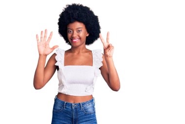 Genç Afro-Amerikalı kadın günlük kıyafetler giyip yedi numaralı parmaklarıyla işaret ederken kendinden emin ve mutlu bir şekilde gülümsüyor.. 