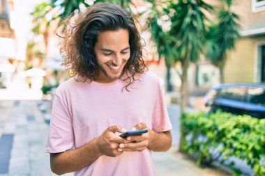 Genç İspanyol adam şehirde akıllı telefon kullanarak mutlu gülümsüyor..