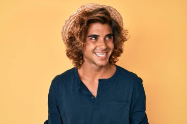 Yaz şapkası takan, yüzünde gülümseme ve doğal ifadeyle yan yana bakan İspanyol bir genç. Kendinden emin gülen. 