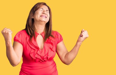 Orta yaşlı güzel bir kadın gündelik giysiler içinde zaferi kutluyor gururlu ve kollarını kaldırarak heyecanla gülümsüyor.