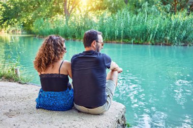 Sıradan kıyafetler giyen orta yaşlı bir çift. Nehrin gerisinde oturuyor, bakıyor ve parmağıyla nehri işaret ediyor..