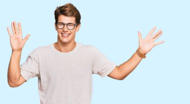 Yakışıklı, beyaz bir adam, günlük kıyafetler ve gözlük takıyor. 10 numarayı gösteriyor ve işaret ediyor. Kendinden emin ve mutlu bir şekilde gülümsüyor.. 