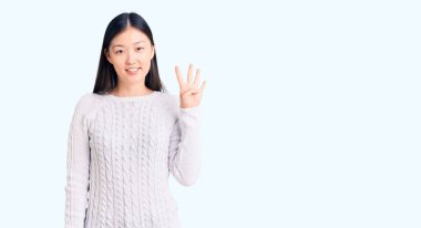 Genç, güzel, Çinli bir kadın gündelik süveter giyer ve parmaklarını dört numaraya uzatarak gülümserken kendinden emin ve mutlu. 