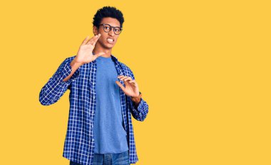 Genç, Afro-Amerikan bir adam günlük kıyafetler ve gözlük takıyor tiksindirici bir ifade takınıyor ve tiksindirici bir yüz ifadesi takınıyor. Eller havada. 