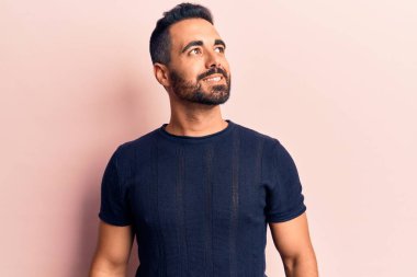 Latin kökenli genç bir adam günlük giysiler giyiyor, rahat bir görünüm takınıyor, doğal bir yüz ifadesi ve kendinden emin bir gülümsemeyle poz veriyor.. 