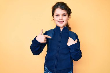 Sırt çantası tutan sevimli İspanyol çocuk gülümseyen mutlu ve gururlu birini işaret ediyor. 