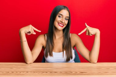 Gündelik kıyafetler giyen genç İspanyol kadın masaya oturmuş kendine güvenen, yüzünde bir gülümsemeyle kendini gururlu ve mutlu bir şekilde gösteriyor.. 