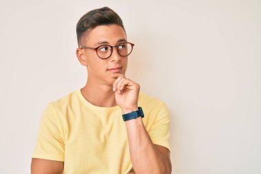 Gündelik kıyafetler ve gözlük takan genç İspanyol çocuk ciddi bir yüzle eli çenesinde soru soruyor, kafa karıştırıcı bir fikir hakkında düşünceli. 