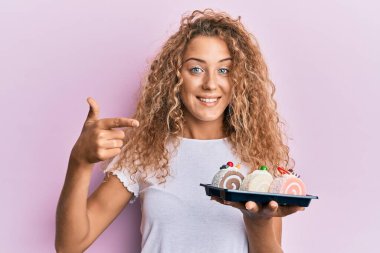 Güzel beyaz kız elinde pasta tatlısı tutarken mutlu bir şekilde elini ve parmağını gösterdi. 
