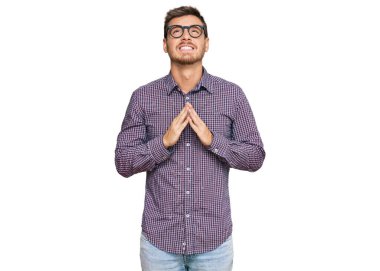 Yakışıklı beyaz adam, günlük kıyafetler ve gözlük takıyor, yalvarıyor ve dua ediyor. Yüzünde umut ifadesi var. Çok duygusal ve endişeli. Yalvarıyor. 