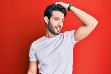 Günlük beyaz tişört giyen genç İspanyol adam gülümsüyor. Kendine güvenen, el hareketleriyle saçlara dokunan, çekici ve modaya uygun poz veren. 