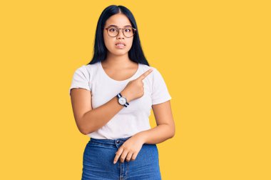 Genç ve güzel Asyalı kız, günlük kıyafetler ve gözlük takıyor endişeli ve gergin bir şekilde işaret ediyor. 