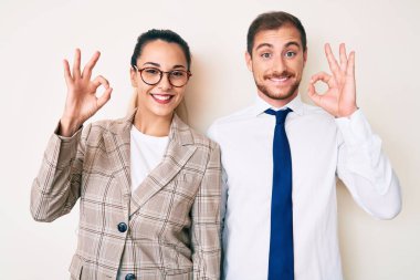 İş kıyafetleri giymiş güzel bir çift pozitif gülümsüyor ve el ve parmaklarıyla imza atıyor. başarılı ifade. 