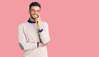 Zarif kıyafetler giyen ve gözlüklü yakışıklı genç adam kameraya kendinden emin bakıyor kollarını kavuşturmuş ve çenesini kaldırmış şekilde gülümsüyor. Olumlu düşünmek. 