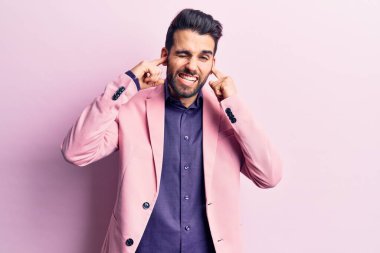 Sakallı, zarif ceketli, kulaklarını parmaklarıyla kapatan, gürültülü müzik sesi için rahatsız edici ifadeleri olan genç yakışıklı bir adam. sağır kavramı. 