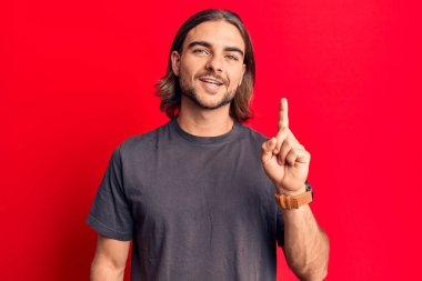 Gündelik kıyafetler giyen genç yakışıklı bir adam bir fikir ya da soruyla gülümsüyor ve mutlu bir yüzle işaret ediyor. 