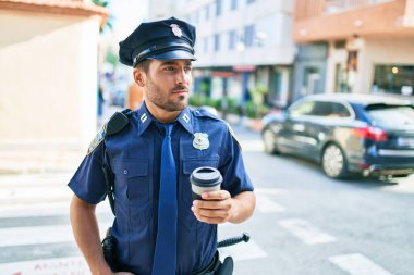 Genç İspanyol polisi ciddi bir ifadeyle polis üniforması giyiyor. Kasaba caddesinde dikilmiş kahve içerken.
