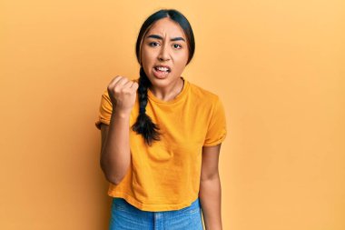 Genç Latin kadın rahat kıyafetler giyiyor kızgın ve kızgın yumruğunu kaldırıyor ve öfkeyle bağırıyor. öfke ve agresif konsept. 